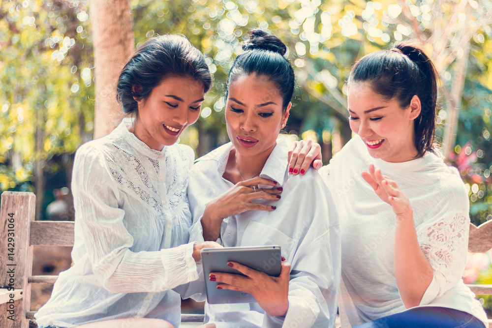 Three beautiful women sitting in a park with a tablet. Three beautiful women sitting in a park with a tablet.