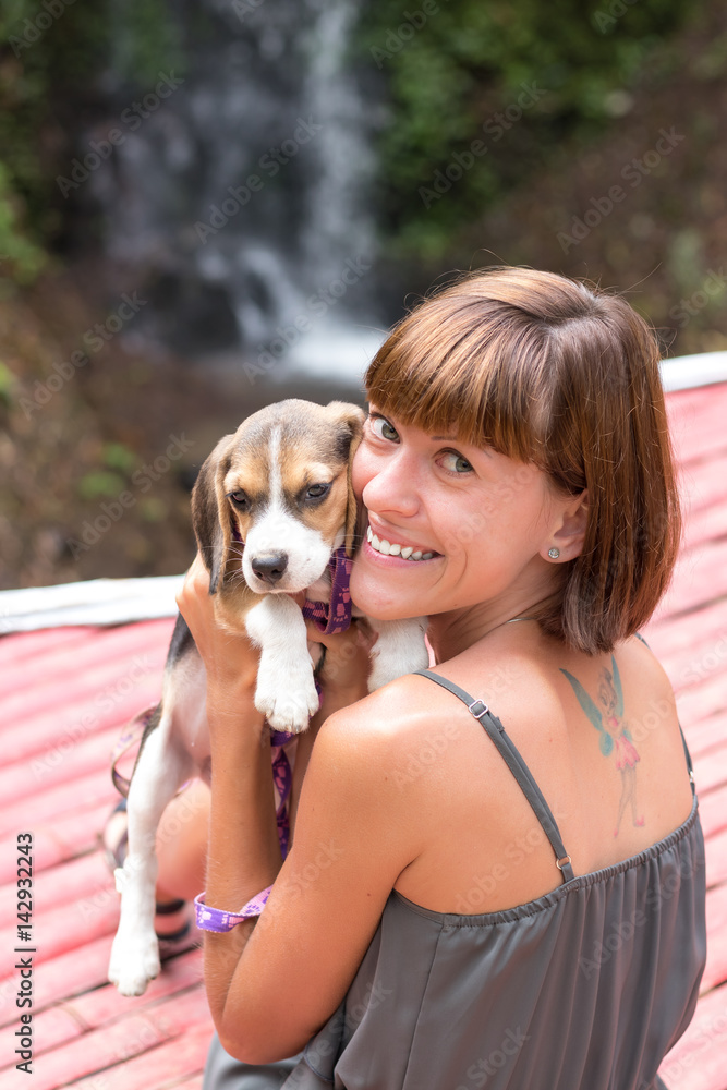 Pretty woman beautiful young happy with small dog puppy beagle. Tropical island Bali, Indonesia. Lady with beagle, waterfall on a background. Love scene. Pretty woman beautiful young happy with small dog puppy beagle. Tropical island Bali, Indonesia. Lady with beagle, waterfall on a background. Love scene.