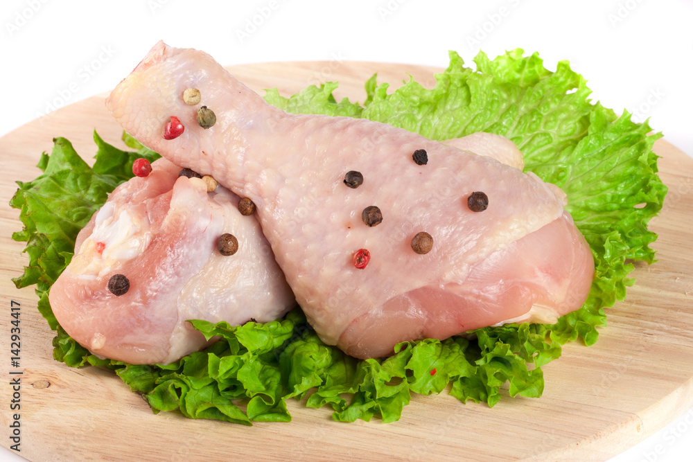 Two raw chicken drumsticks with lettuce leaf on a wooden cutting board isolated on white background Two raw chicken drumsticks with lettuce leaf on a wooden cutting board isolated on white background