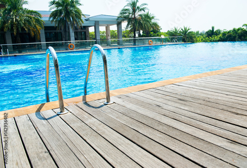 Swimming pool with stair and wooden deck at hotel.