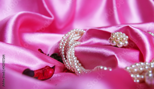 Beautiful pearls on a background of pink silk. Fashion & Style. Necklace and earrings.