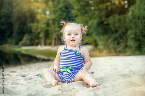 Fototapeta Naklejka Na Ścianę i Meble -  Cheerful baby girl sitting on the sand. The concept of childhood, leisure and lifestyle.