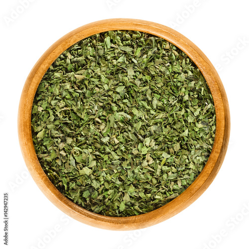 Dried and grated lovage leaves in wooden bowl. Edible green herb and vegetable, used in salads and soups. Levisticum officinale. Isolated macro food photo close up from above on white background.