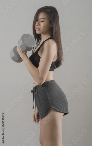  portrait of fit sexy girl  wearing sportswear fitness clothing exercise weights lifting on gray background