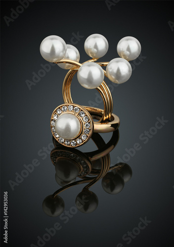 Two jewelry rings with pearls on black background with reflection