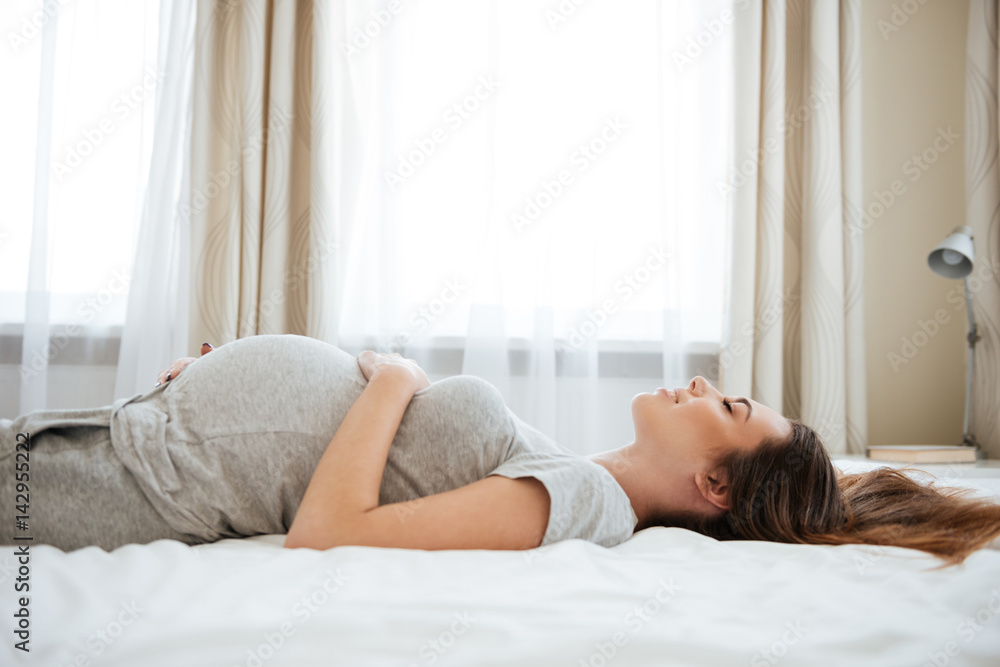 Smiling pregnant young woman lying and relaxing on bed Smiling pregnant young woman lying and relaxing on bed