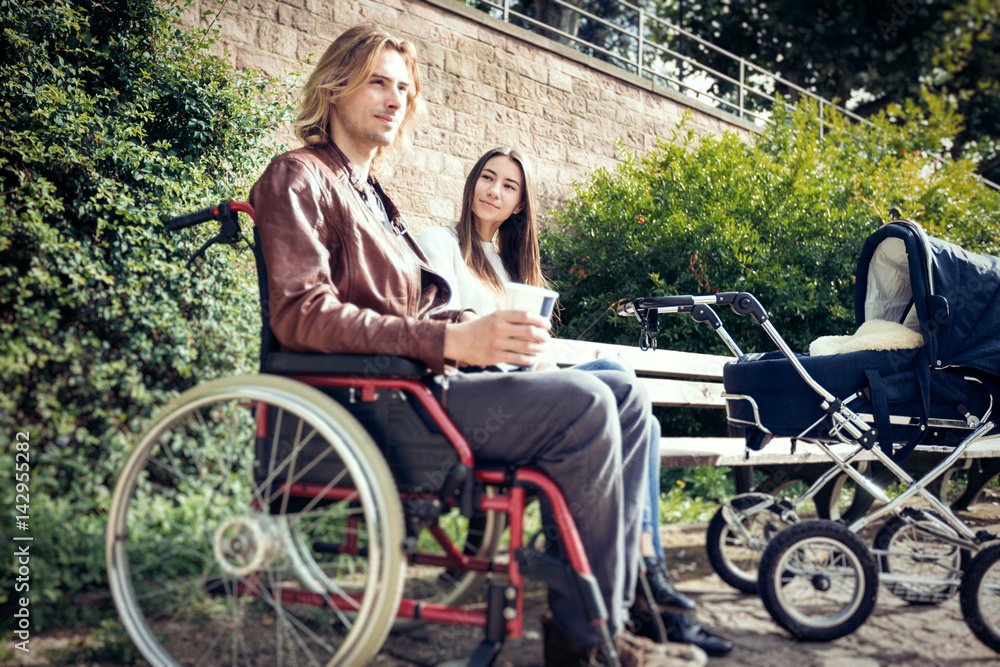 Young Parents In Wheelchair With Baby Stroller In The Park Young Parents In Wheelchair With Baby Stroller In The Park