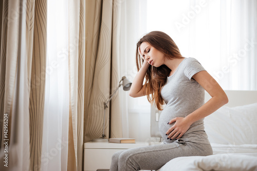 Sad pregnant woman having headache and feeling sick on bed