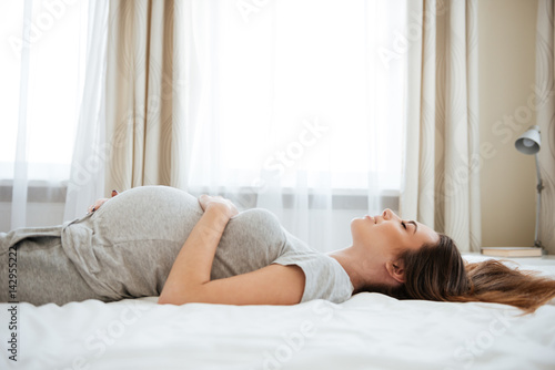 Billede på lærred Smiling pregnant young woman lying and relaxing on bed