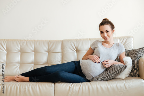 Cheerful attractive pregnant young woman lying and relaxing on sofa