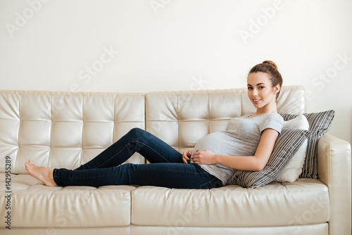 Smiling pretty pregnant young woman lying and resting on sofa