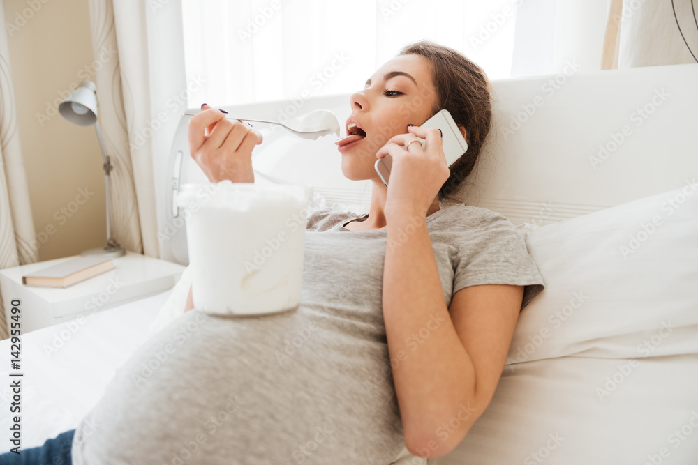 Pregnant woman eating ice cream and talking on mobile phone Pregnant woman eating ice cream and talking on mobile phone