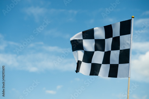 checkered race flag waving on blue sky.