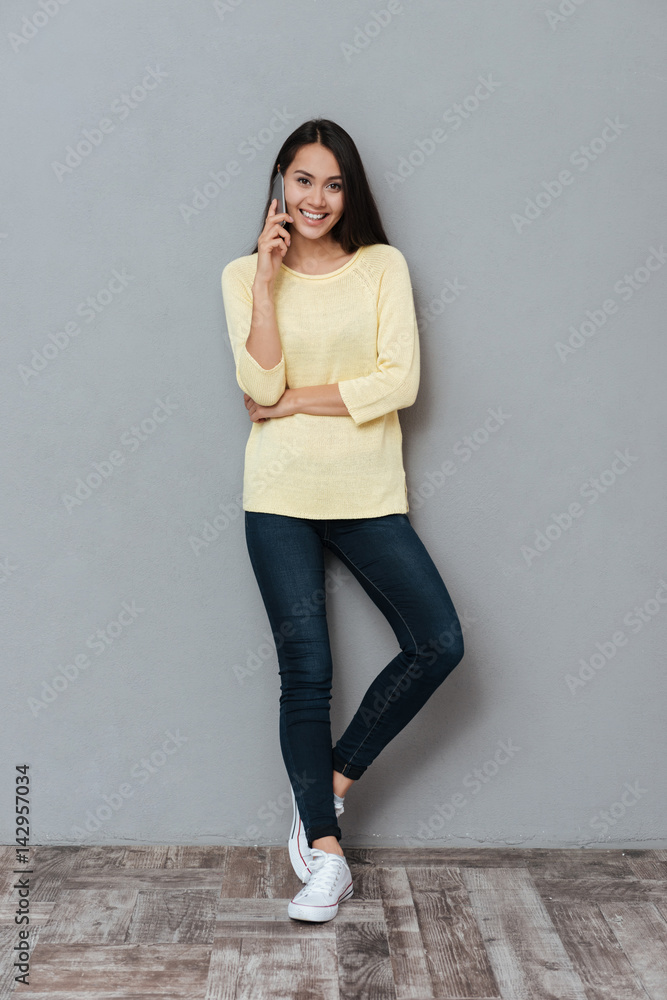 Full length of cheerful young woman talking on mobile phone
