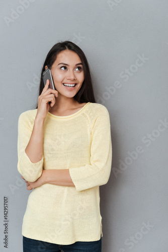 Cheerful cute young woman standing and talking on cell phone