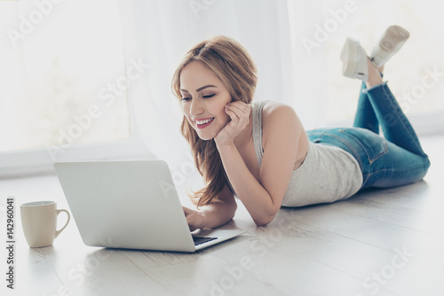 Pretty smiling cute girl lying on the floor and using laptop