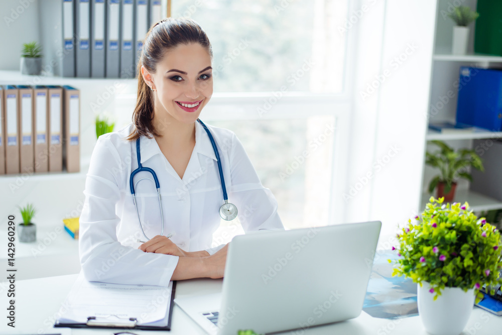 Horizontal photo of young smiling therapist sitting at the table at her medical office Horizontal photo of young smiling therapist sitting at the table at her medical office