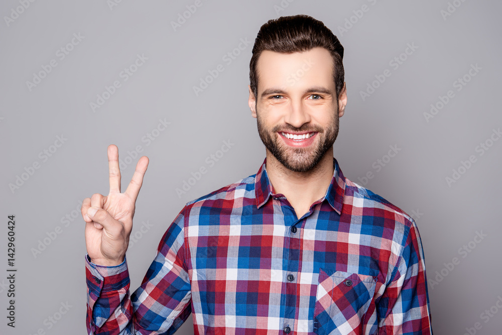 A horizontal portrait of young bearded man showing v-sign against gray background A horizontal portrait of young bearded man showing v-sign against gray background