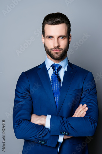Portrait of serious fashionable handsome man in blue suit and tie crossing hands and look at camera
