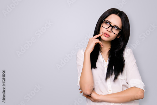 Young successful woman in spectacles has new idea and think about it. She looks to the side on copy space