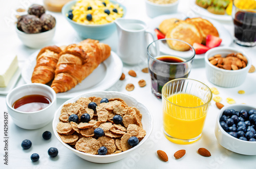 Breakfast table setting with flakes, juice, croissants, pancakes and fresh berries