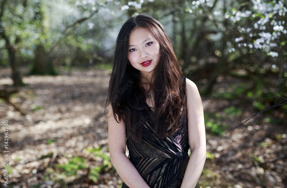 Portrait of a beautiful Chinese, Oriental woman with beautiful eyes and long dark hair posed against a woodland background with blossom trees Portrait of a beautiful Chinese, Oriental woman with beautiful eyes and long dark hair posed against a woodland background with blossom trees