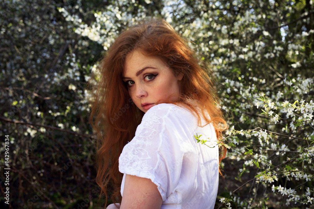 Beautiful portrait of a young woman with long red hair, freckles and sultry pensive looks, set against a woodland background with white blossom Beautiful portrait of a young woman with long red hair, freckles and sultry pensive looks, set against a woodland background with white blossom