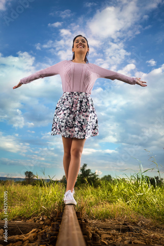Cheerful young woman with outstretched arms is walking on railroad track