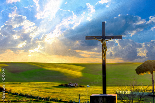 Jesus Christ on the cross by the road in the fields at sunset, with drammatic clouds and sun rays on the sky. photo