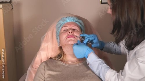 The physician of the cosmetologist removes the raised tonus of muscles by means of a prick of botulotoxin. The doctor injects Botox into the nasolabial part of the face to eliminate facial wrinkles photo