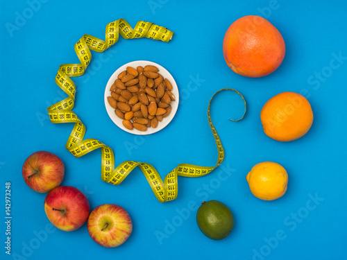 Fototapeta Naklejka Na Ścianę i Meble -  Diet concept: grapefruit, orange, lemon, lime, almond, apples and measuring tape on blue background. Top view
