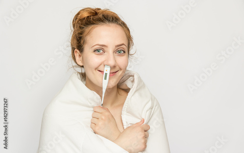 Young funny woman in blanket with thermometer in her nose. Sick girl with a thermometer on a white background, flu, colds photo