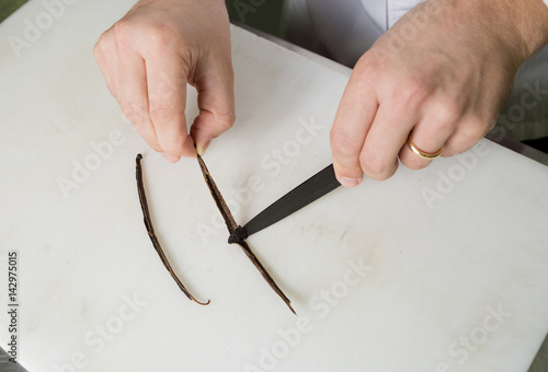 A vanilla pod on a white chopping board, being scraped by a sharp knife to extract the vanilla essence. photo