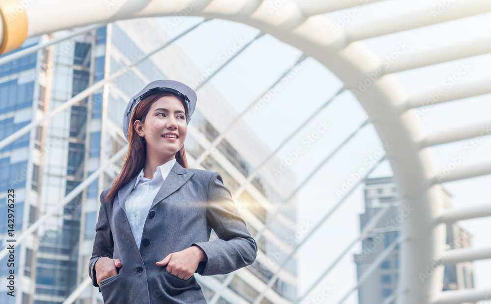 Portrait of beautiful young engineer woman wear a white safety helmet smiling with commitment to success at downtown with building background Portrait of beautiful young engineer woman wear a white safety helmet smiling with commitment to success at downtown with building background