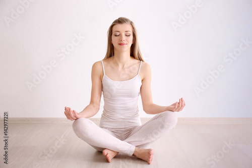 Beautiful young woman meditating while sitting on floor at home