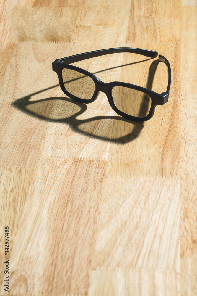 Black eyeglasses lay on wood table with shadow near window,leave space for adding your text