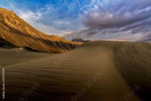 sand dunes against the background of distant colorful mountain range and sunrise sky  Ladakh  Himalaya  Jammu   Kashmir  Northern India