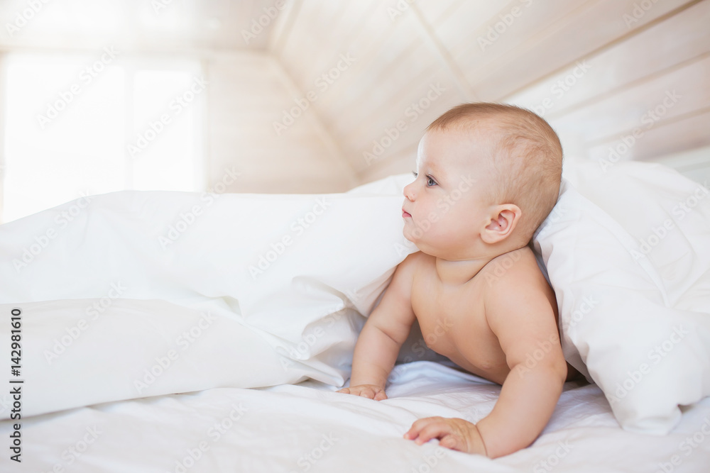 Little baby looks out to a side from a blanket on a white bed Little baby looks out to a side from a blanket on a white bed