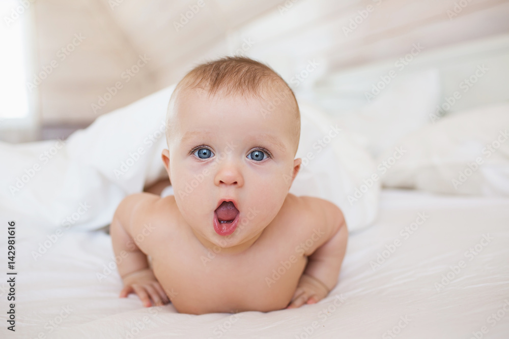 Portrait of little baby lies on a white bed and open her mouth Portrait of little baby lies on a white bed and open her mouth