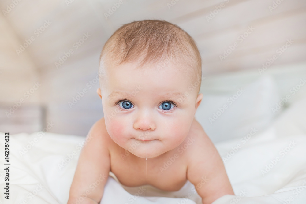 Portrait of infant with slobbers on a white bed in bedroom Portrait of infant with slobbers on a white bed in bedroom