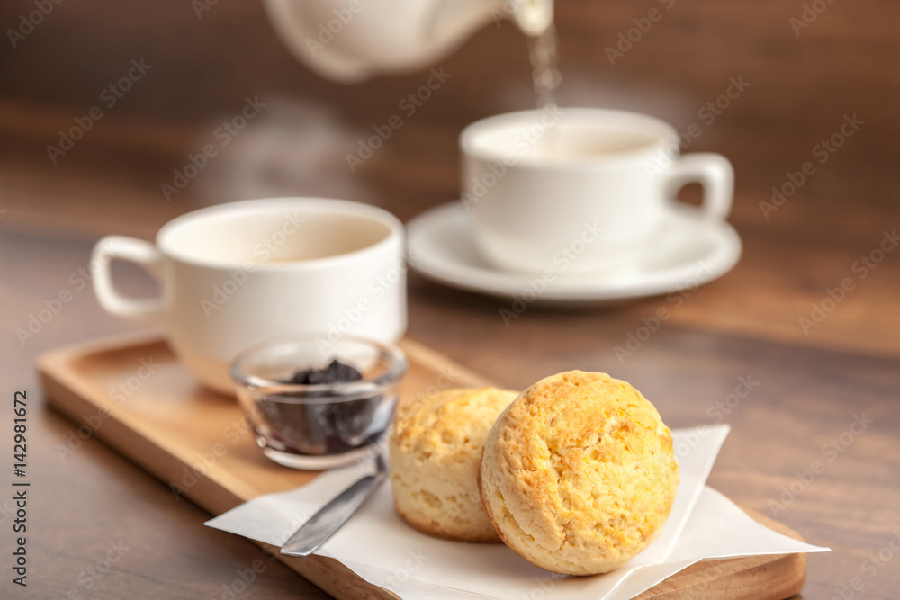 Cups of tea served with scones and homemade blueberry jam on wooden background (selective focus)