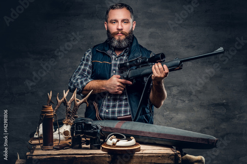 Bearded modernl hunter with his trophy holds a rifle.