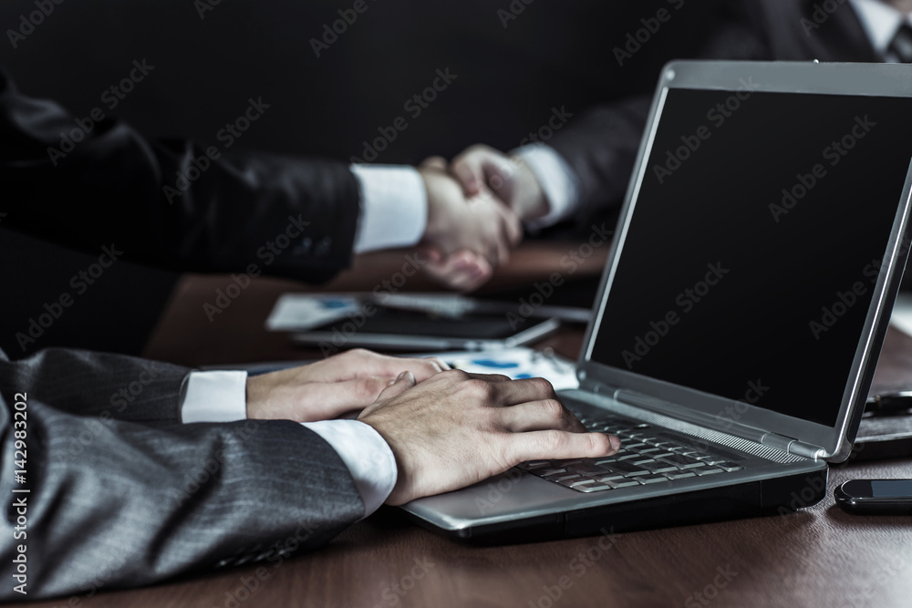 closeup of businessman working on laptop on background of business partners handshaking closeup of businessman working on laptop on background of business partners handshaking