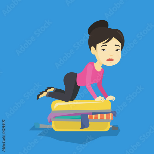 Young woman trying to close suitcase.