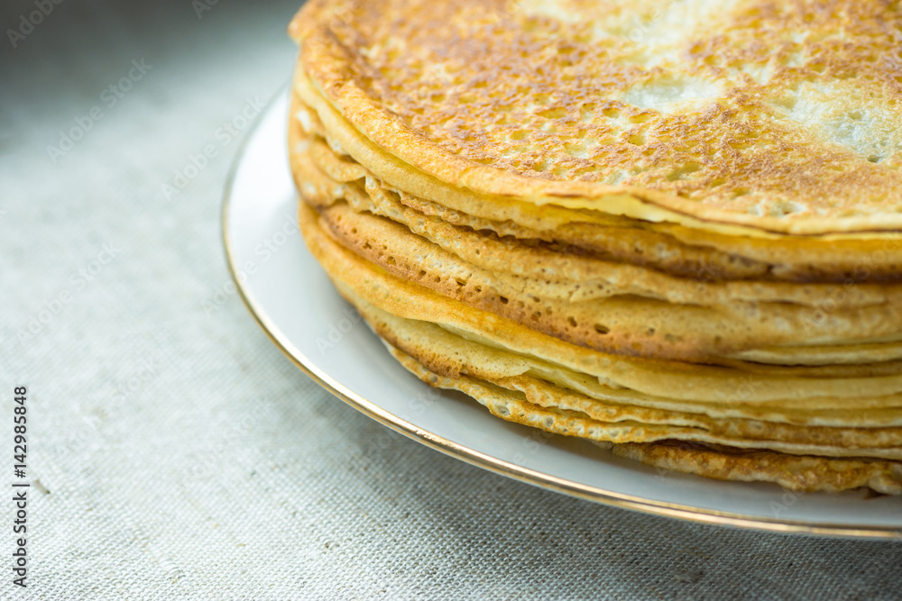 Stacked golden crepes on white plate on linen cloth background, breakfast, cozy morning atmosphere Stacked golden crepes on white plate on linen cloth background, breakfast, cozy morning atmosphere