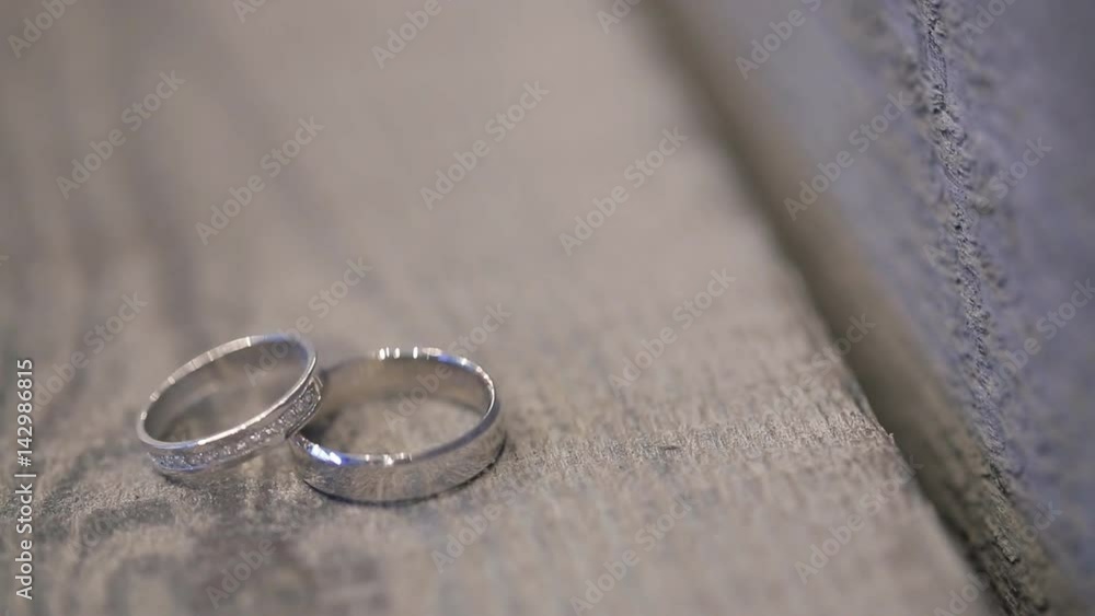 two white golden rings on photo shoot on wooden table outdoors in wedding day. gold ring for bride with brilliants, diamonds, wide accessorise groom before ceremony. Main accessories for newlyweds to two white golden rings on photo shoot on wooden table outdoors in wedding day. gold ring for bride with brilliants, diamonds, wide accessorise groom before ceremony. Main accessories for newlyweds to