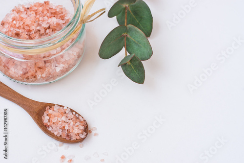 Pink Himalayan salt in glass jar, green eucalyptus branch, wooden spoon on white background, spa, wellness, health concept photo