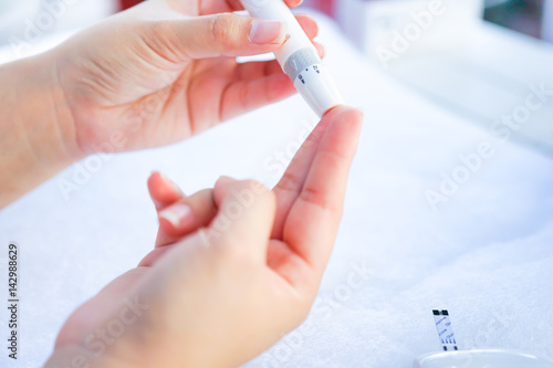 Asian woman hands using lancet on finger to check blood sugar test level by Glucose meter  Healthcare Medical and Check up  Medicine  diabetes  glycemia  health care and people concept