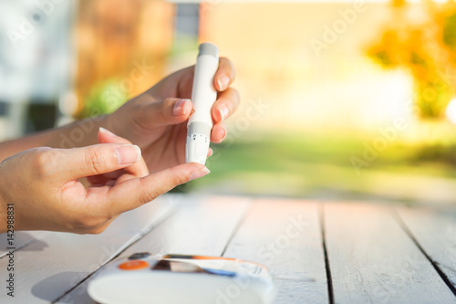 Foto Asian woman hands using lancet on finger to check blood sugar test level by Gluc