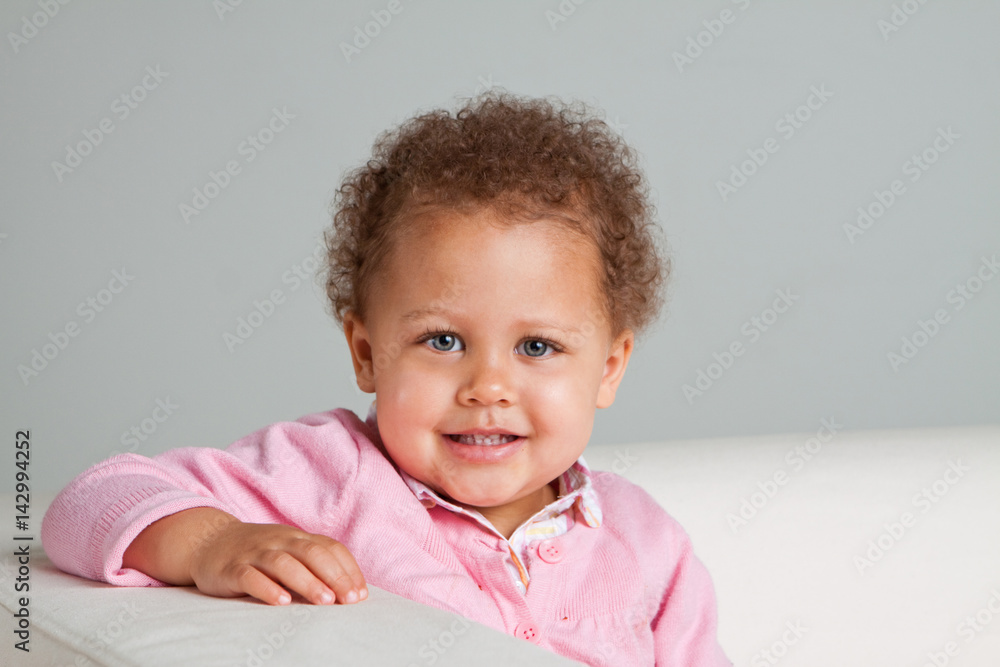 Cute mixed raced little girl smiling sitting on a sofa. Cute mixed raced little girl smiling sitting on a sofa.
